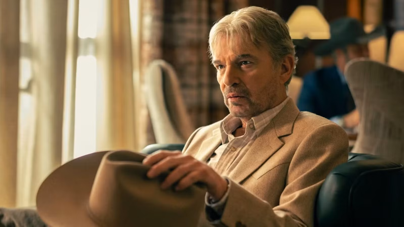 Billy Bob Thornton as Tommy Norris sitting in a chair, holding his hat and talking in Landman.