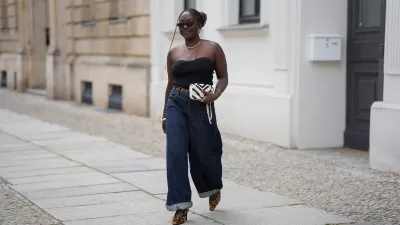 BERLIN, GERMANY - JULY 4: Lois Opoku is seen wearing a black ribbed strapless top with a sweetheart neckline from Uniqlo; dark blue high waist wide leg denim jeans with turned up cuffs from Levi’s; a slim leopard print belt from H&M Studio; leopard print pointed toe Mary Jane pumps from H&M Studio; a Chanel Mini CC bicolor chevron stitched lambskin flap shoulder bag with a gold tone chain strap; a gold collar necklace from Alexis Bittar and a gold pendant necklace from Bruna the Label; gold hoop earrings from ASOS; gold cuff bracelets and a gold chain bracelet from Petite Villa Mauresque; rings from Pandora and Maria Black; oval tortoiseshell frame sunglasses with dark tinted lenses from Corlin during the Berlin Fashion Week Spring/Summer 2026 on July 4, 2026 in Berlin, Germany. (Photo by Moritz Scholz/Getty Images)