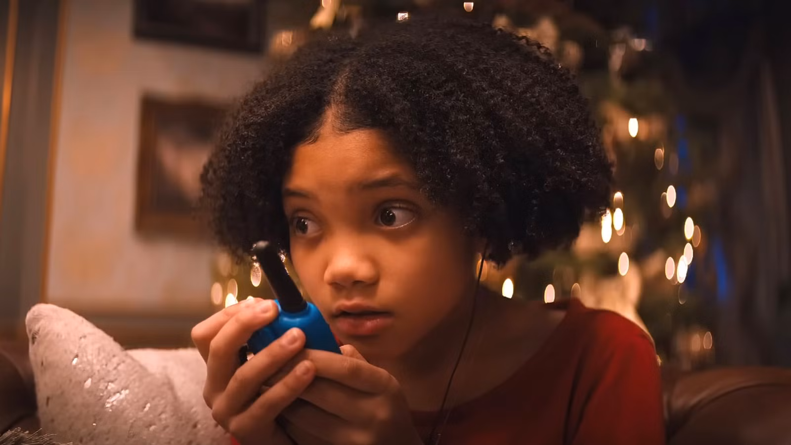 Leah Brady talking into a walkie talkie with a Christmas tree behind her - Violent Night