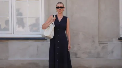 COPENHAGEN, DENMARK - AUGUST 6: Justyna Czerniak wears black sunglasses, gold earrings, black tailored vest midi dress, gold necklace, gold rings, cream DeMellier leather bag, black Alaia sheer mesh ballet flats, outside Lovechild 1979, during the Copenhagen Fashion Week Spring/Summer 2024-2025 on August 6, 2024 in Copenhagen, Denmark. (Photo by Edward Berthelot/Getty Images)