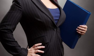a professional woman holds a folder; she is wearing a blazer and does in fact look busty