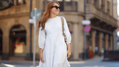 A young woman in a white dress walks through the streets of the city. People, fashion, lifestyle, travel and vacations concept