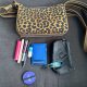 image of what's in Kat's bag on July 1, 2026: black pouch, blue wallet, blue hair clip, purple mirror with elastic wrapped around it, 2 lip glosses, concealer, and a (very old) pill case. The purse itself is leopard from Rothy's.
