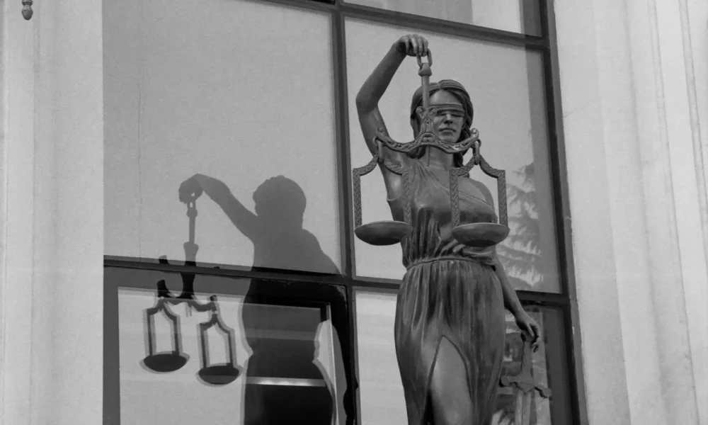 A statue of Lady Justice holding scales in front of a window.