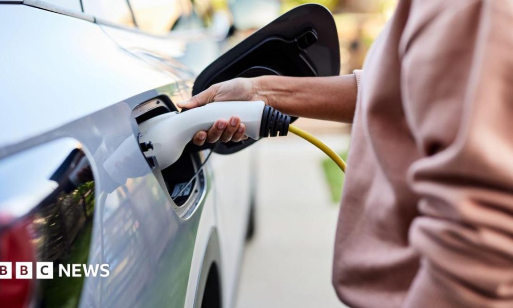 A woman plugs a charging cable into a grey electric car.