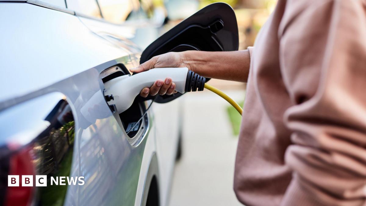 A woman plugs a charging cable into a grey electric car.