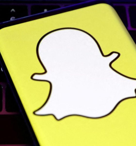 A closeup of Snapchat's logo, a white cartoon ghost with a bright yellow background, held over a laptop conputer keyboard.