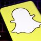 A closeup of Snapchat's logo, a white cartoon ghost with a bright yellow background, held over a laptop conputer keyboard.
