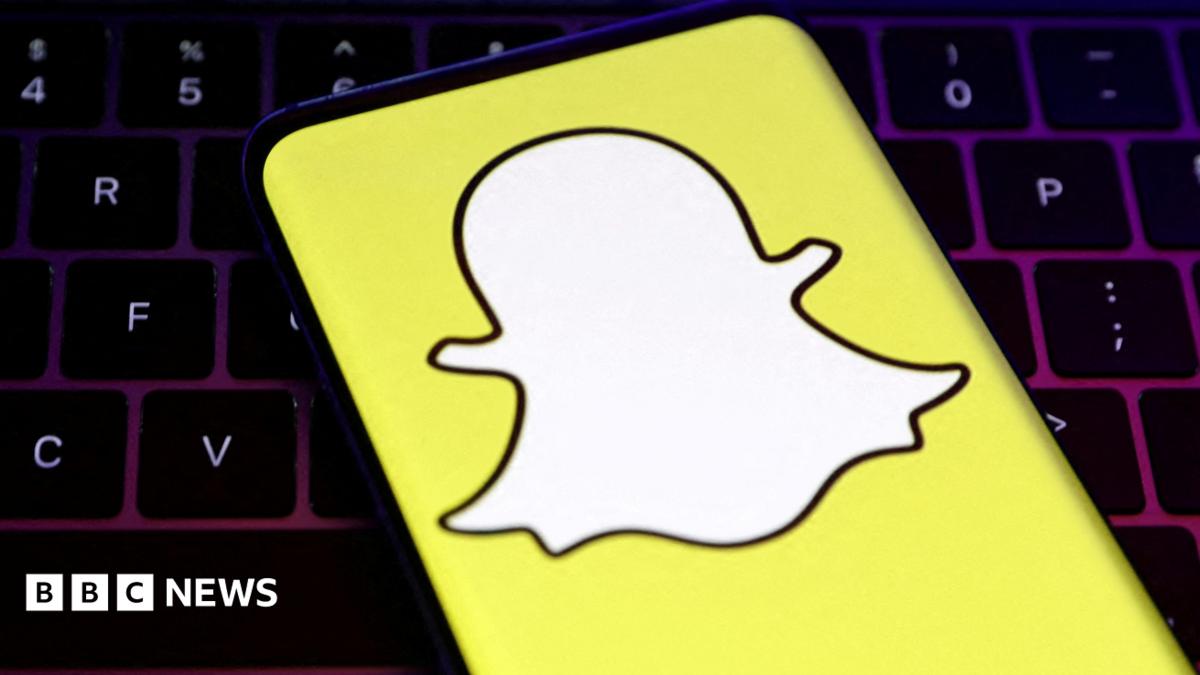 A closeup of Snapchat's logo, a white cartoon ghost with a bright yellow background, held over a laptop conputer keyboard.