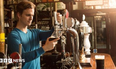A man wearing a blue top pouring a pint in a pub