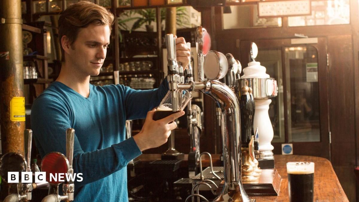 A man wearing a blue top pouring a pint in a pub