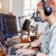 A tech worker with pink hair sits at a desk and works on a laptop