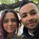A selfie of a man and a woman sitting beneath a tree.