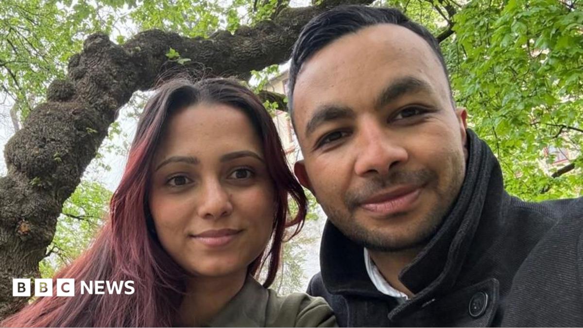 A selfie of a man and a woman sitting beneath a tree.