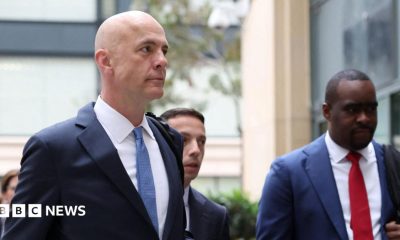 Close up of Mark Zuckerberg wearing a suit, looks towards the camera with a blank expression. He is flanked by staff also in suits. Photographed in February 2026