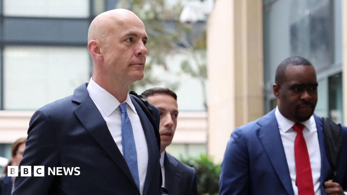 Close up of Mark Zuckerberg wearing a suit, looks towards the camera with a blank expression. He is flanked by staff also in suits. Photographed in February 2026