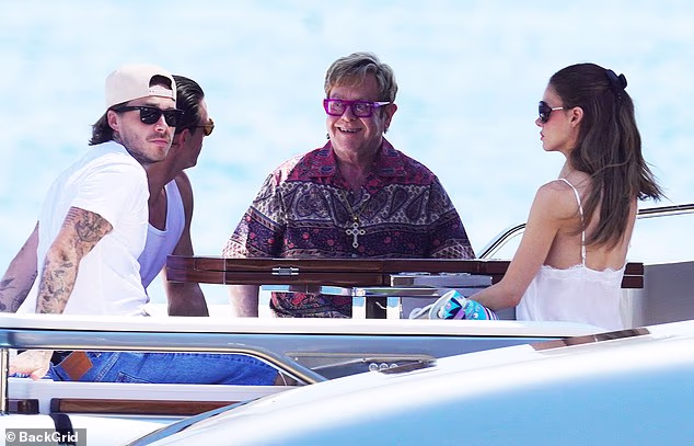 Brooklyn Beckham and Nicola Peltz were pictured in the South of France with his godfather Elton John, just miles away from his estranged parents on Saturday