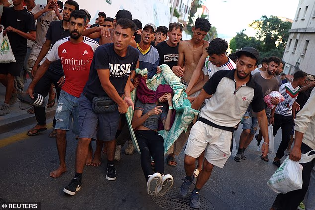Migrants carry a fellow migrant, who they say was injured when the Spanish police and military tried to contain the migrants to an area of a beach