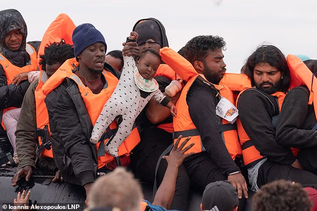 A man holds a baby in a babygrow as migrants board a dinghy at the beach at Ecault in France