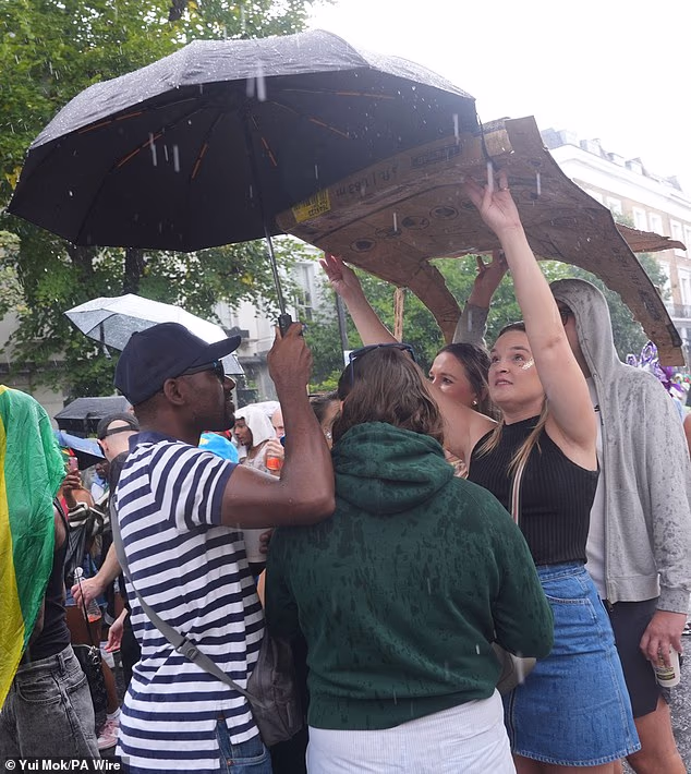 Revellers held up umbrellas and cardboard to shield themselves from the rain on family day at the Notting Hill Carnival