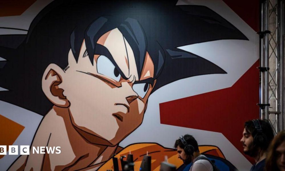 A graphic from the Dragon Ball Z comic is seen displayed on a wall above several people on computers