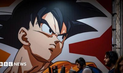 A graphic from the Dragon Ball Z comic is seen displayed on a wall above several people on computers