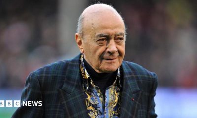 Al Fayed is wearing a suit jacket as he walks across a football pitch