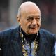 Al Fayed is wearing a suit jacket as he walks across a football pitch