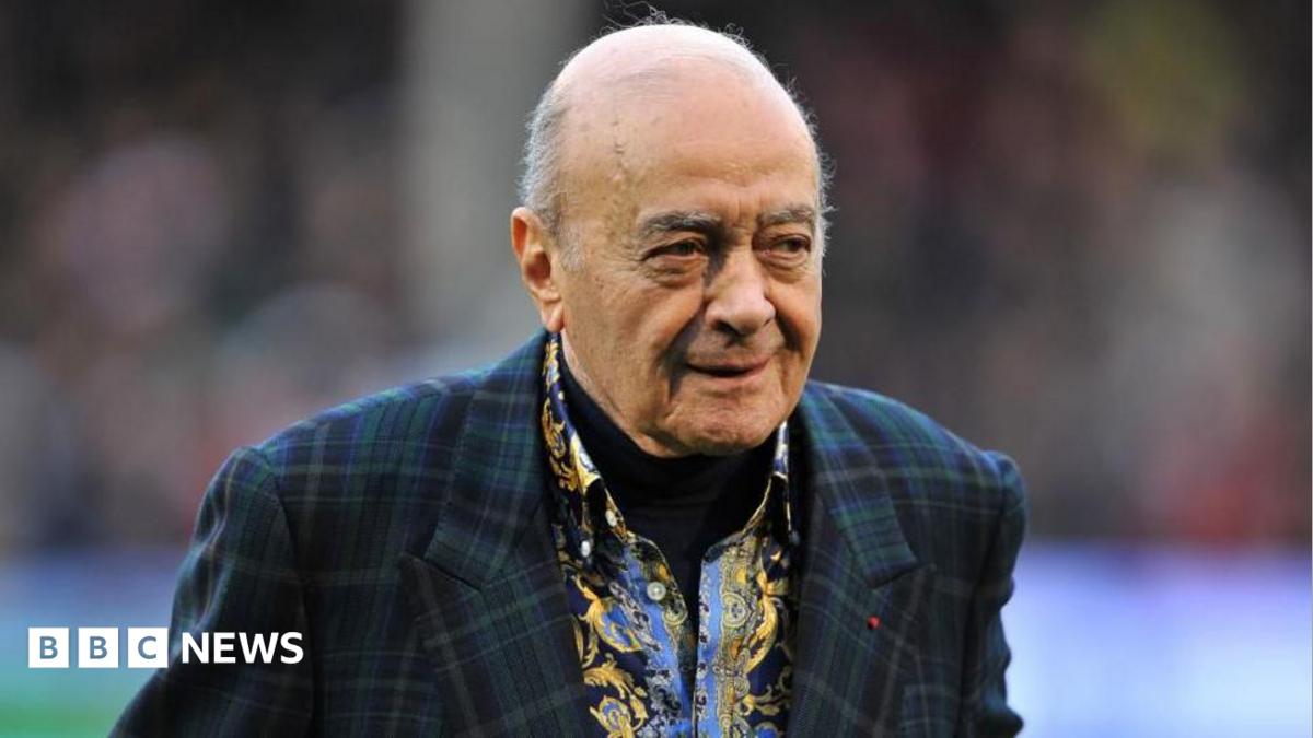 Al Fayed is wearing a suit jacket as he walks across a football pitch