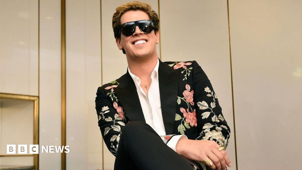 Milo Yiannopoulos wears a colourful suit with dark glasses and a white shirt.