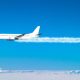 A jet plane flies across the blue sky, with white contrails coming from its engines