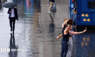 wet street with a man walking along with an umbrella and two women posing for selfie in the rain