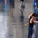 wet street with a man walking along with an umbrella and two women posing for selfie in the rain