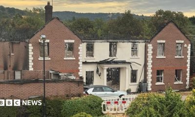 A large building with white pillars, significantly destroyed by fire. The roof has burnt away and much of the back of the building, as visible through the door and many windows.