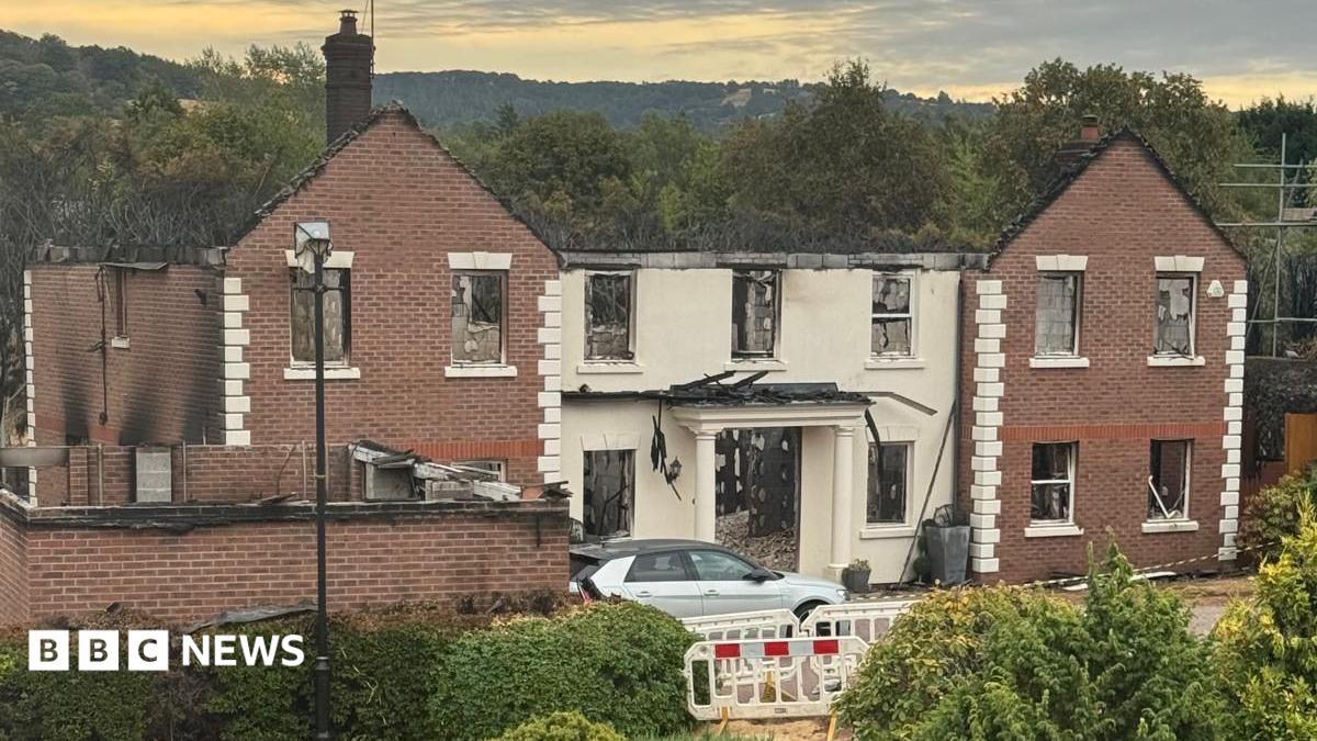 A large building with white pillars, significantly destroyed by fire. The roof has burnt away and much of the back of the building, as visible through the door and many windows.