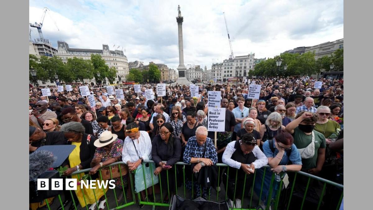 A crowd of people gather in Trafalgar Square as part of a vigil for Jason Arday. Some of them are holding placards.