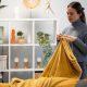 Woman arranging a warm, soft yellow blanket on a sofa