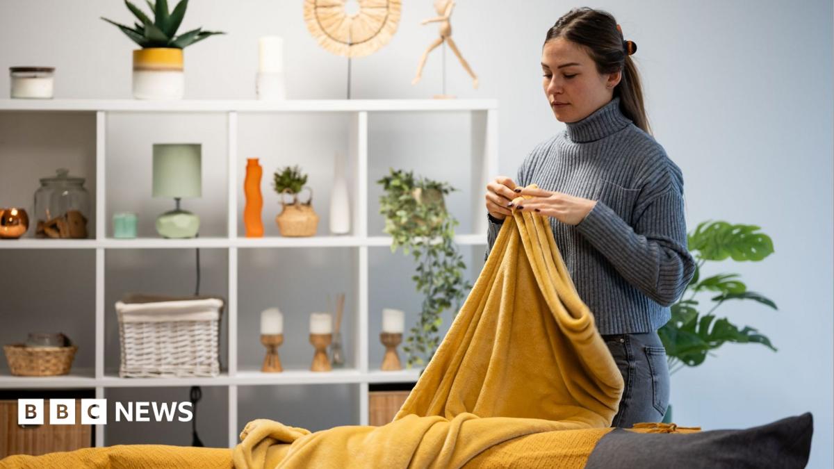 Woman arranging a warm, soft yellow blanket on a sofa