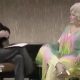 A man in a dark suit interviewing a woman in a colourful outfit.