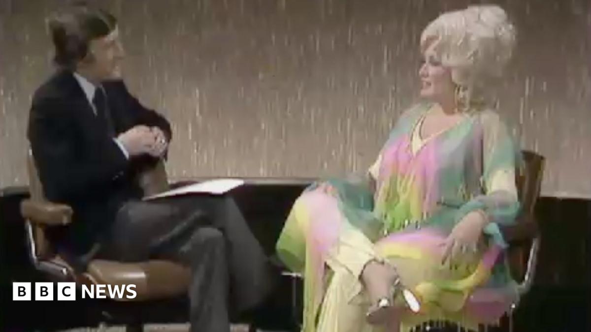 A man in a dark suit interviewing a woman in a colourful outfit.
