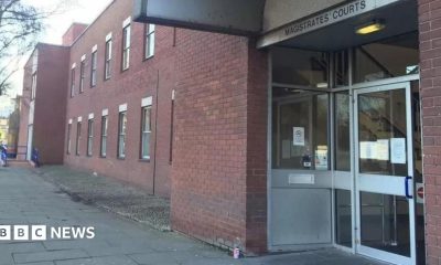 A red-bricked double-storey building with a large glass door. Above the door is a sign that reads: "Magistrates' Courts". There are paving slabs leading up to the entrance.