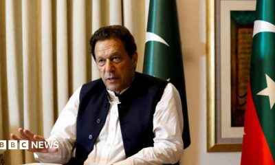 Former Pakistani Prime Minister Imran Khan speaks with Reuters during an interview, in Lahore, Pakistan March 17, 2023. He can be seen seated with his hand outstretched and speaking. Two Pakistani flags are behind him