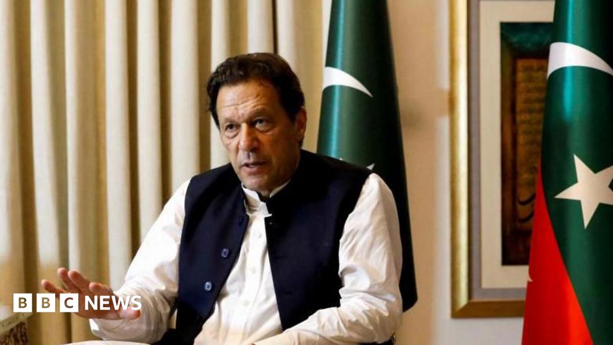 Former Pakistani Prime Minister Imran Khan speaks with Reuters during an interview, in Lahore, Pakistan March 17, 2023. He can be seen seated with his hand outstretched and speaking. Two Pakistani flags are behind him