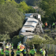 Three train carriages that have derailed. Several emergency workers are congregating by the side of the railway.
