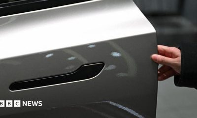 A customer inspects the minimalistic hidden door handles on an electric car in a showroom.
