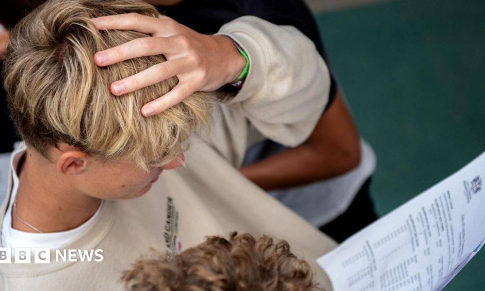 A student with blonde hair holds their hand to their head as they look at their GCSE results at the City of London Freemen's School