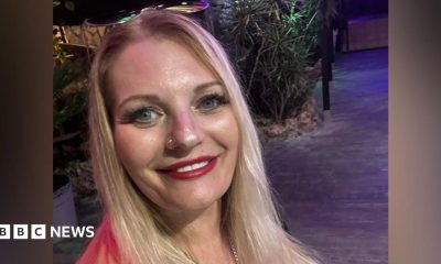 Head-and-shoulders of Michaela Wilson who has long, straight blonde hair, blue eyes, red lipstick and has a pair of sunglasses on top of her head.
