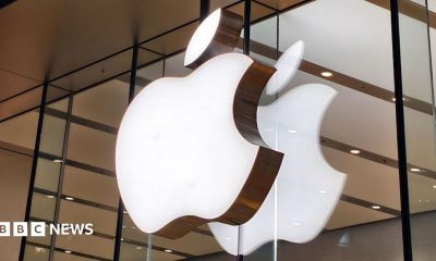 Apple logo lit up on a sign on the glass windows of a storefront in China.