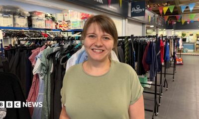 Ashleigh Hirst standing in the charity's uniform store, smiling at the camera. She has brown hair tied back and a fringe. She is wearing a green T-shirt.