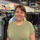 Ashleigh Hirst standing in the charity's uniform store, smiling at the camera. She has brown hair tied back and a fringe. She is wearing a green T-shirt.